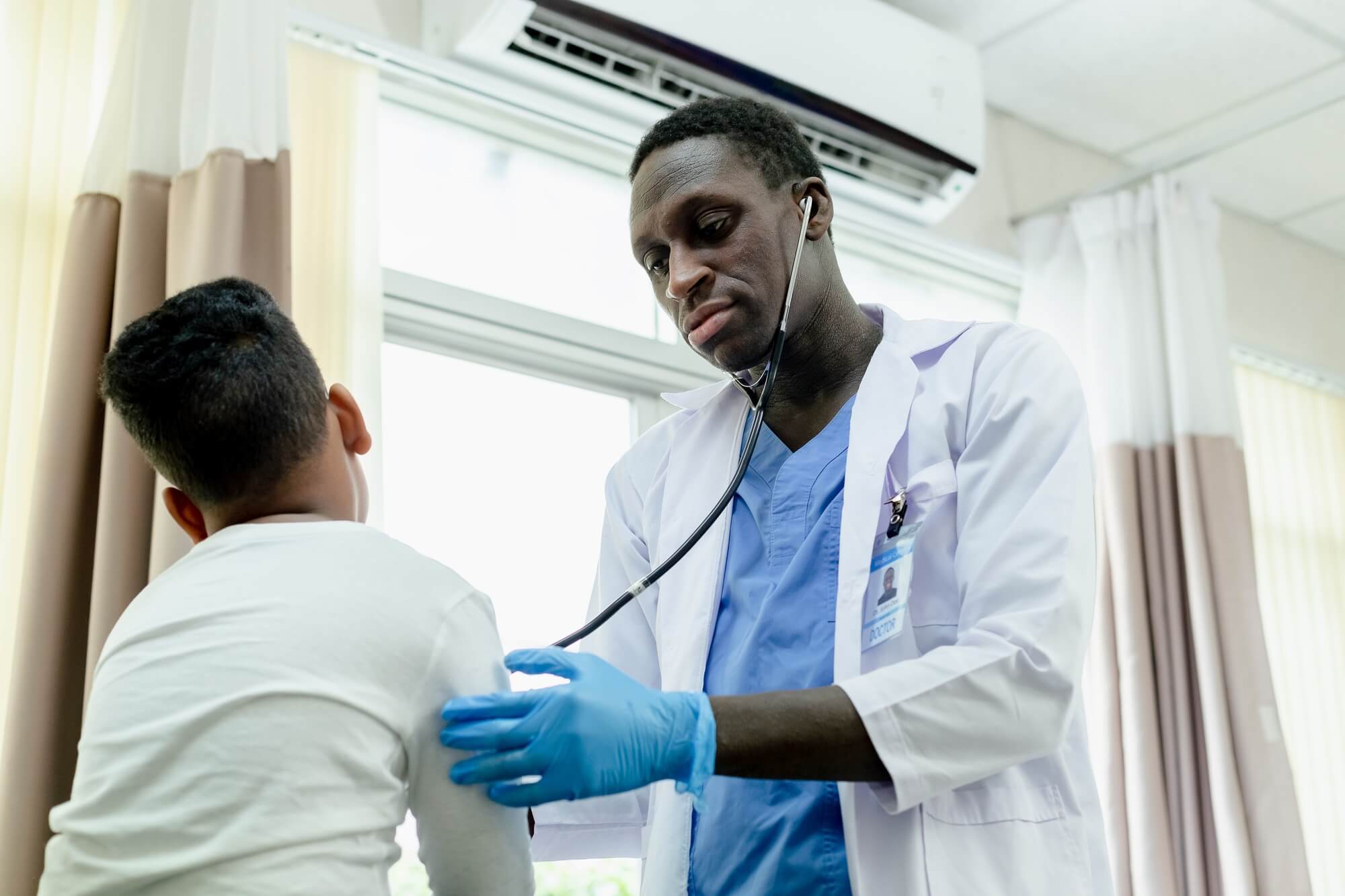 African American medical male doctor use stethoscope checkup diagnosis child boy patient.